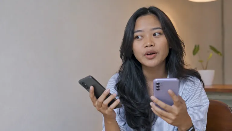 Perempuan membandingkan dua HP di kafe