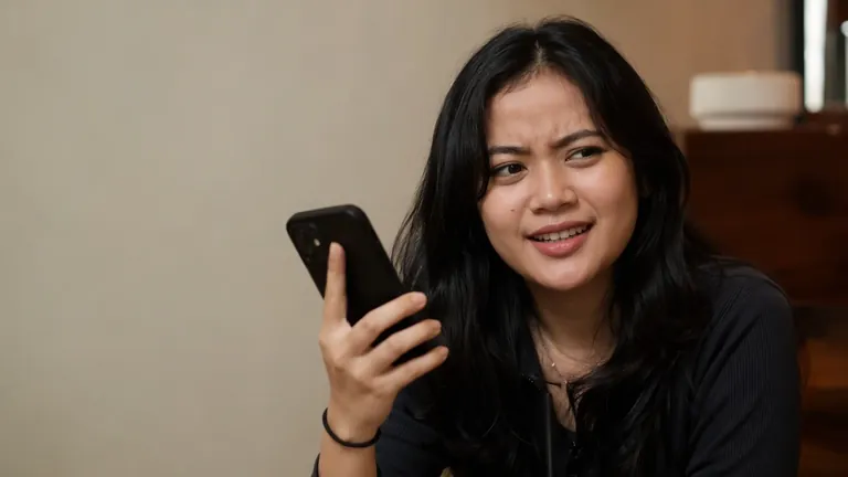 Perempuan menyipitkan mata dengan ragu melihat HP di kafe