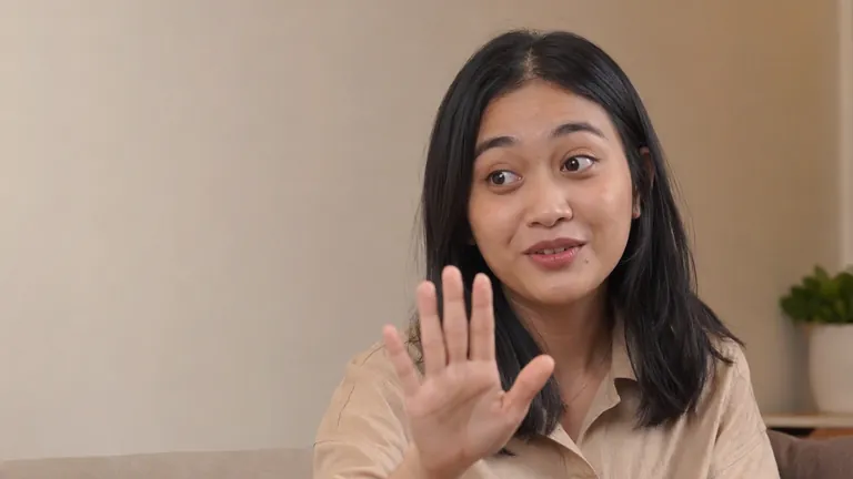 Perempuan di ruang podcast mengangkat telapak tangan ke kamera