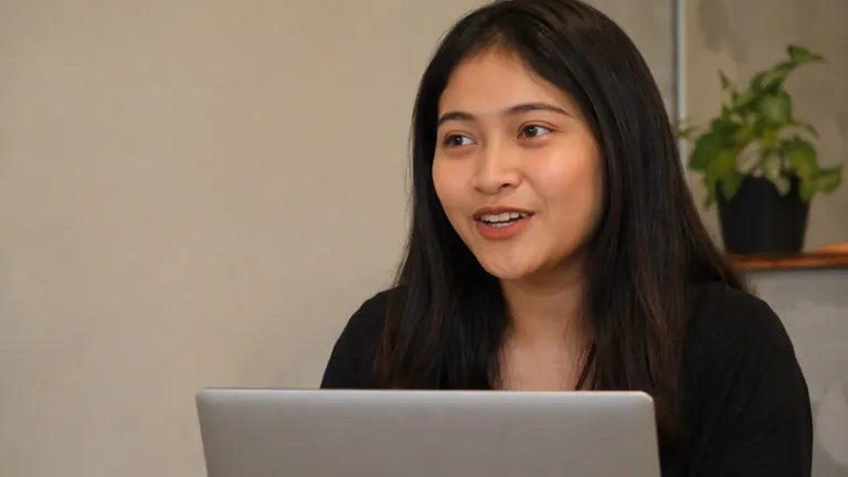 Perempuan tersenyum bekerja di laptop perak