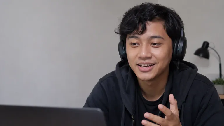 Clipper berheadphone tersenyum di depan laptop
