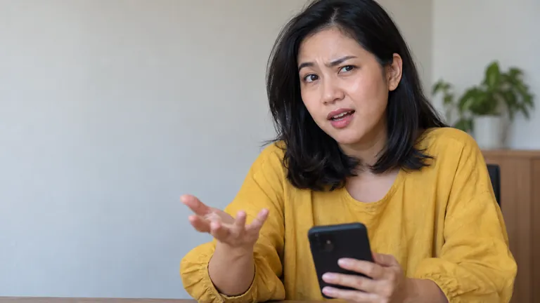 Perempuan memegang HP dengan wajah bertanya