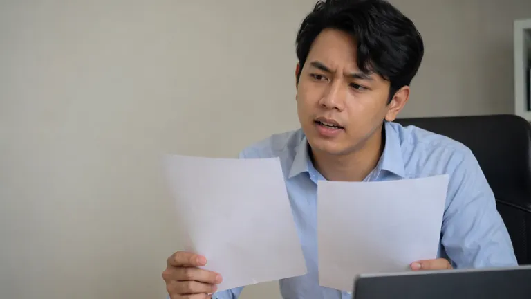 Pria berkemeja membandingkan dua lembar kertas