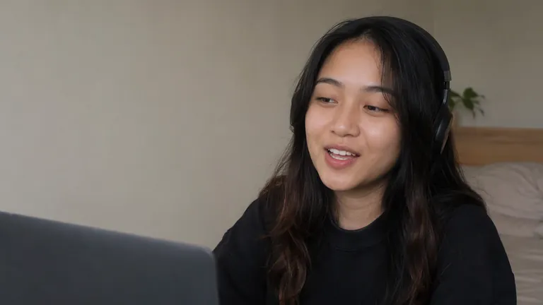 Perempuan berheadphone tersenyum di depan laptop