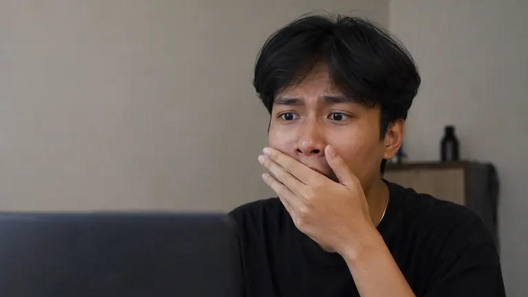 Pria kaget menutup mulut di depan laptop
